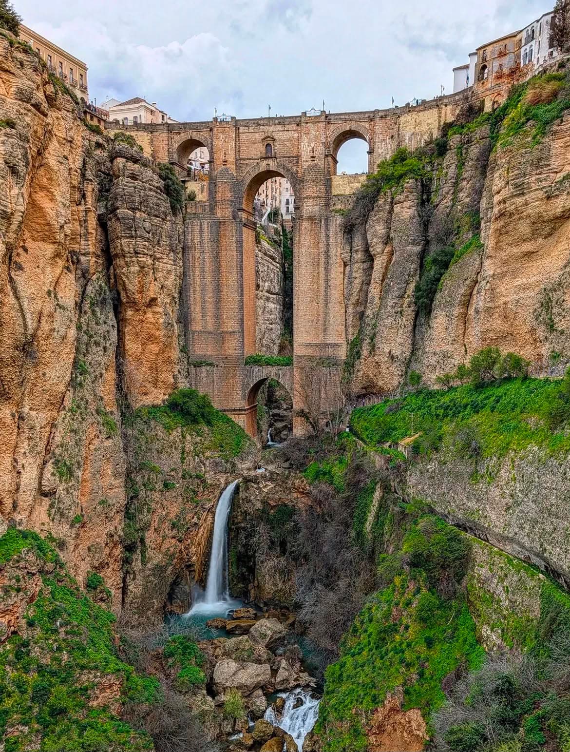 Een hoge stenen brug over een diepe kloof, met een waterval eronder